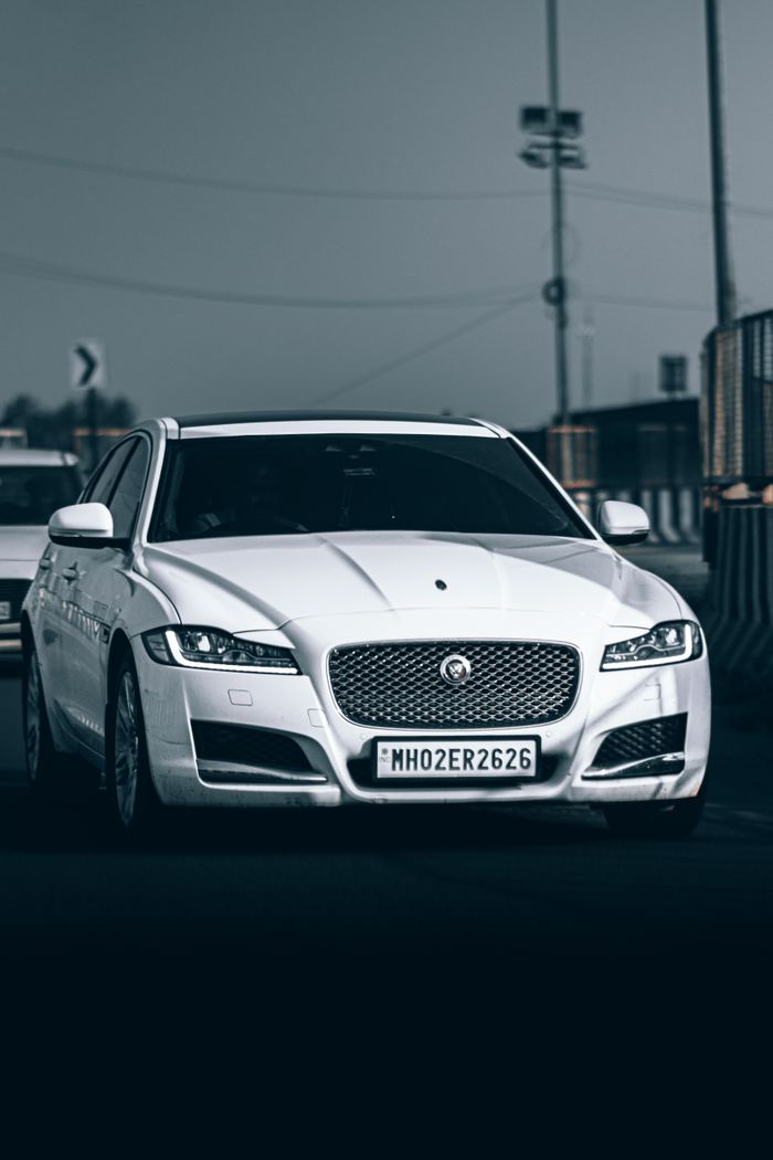 White luxury car driving on a city road, showcasing elegance and speed in an urban setting.